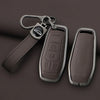 A dark brown leather key case cover with a metal fob and chain attached, shown against a dark background.