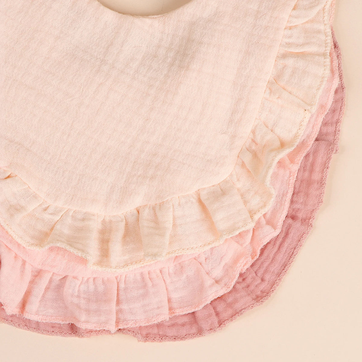 A set of three soft cotton ruffle bibs in shades of pink and mauve.