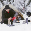 A person is cooking in a pot outdoors next to a tent in the snow using an adjustable aluminum camping stove.