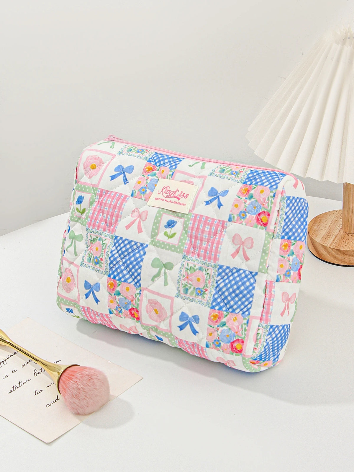 A pink and blue patchwork quilted makeup bag with floral and polka dot patterns rests on a white surface.