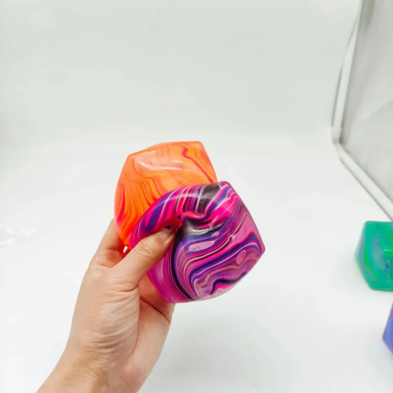 Une main tient un cube de jeu en gel anti-stress marbré orange et violet.