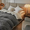 A luxurious gray velvet duvet cover and blanket with white pillows on a bed in a bright room.