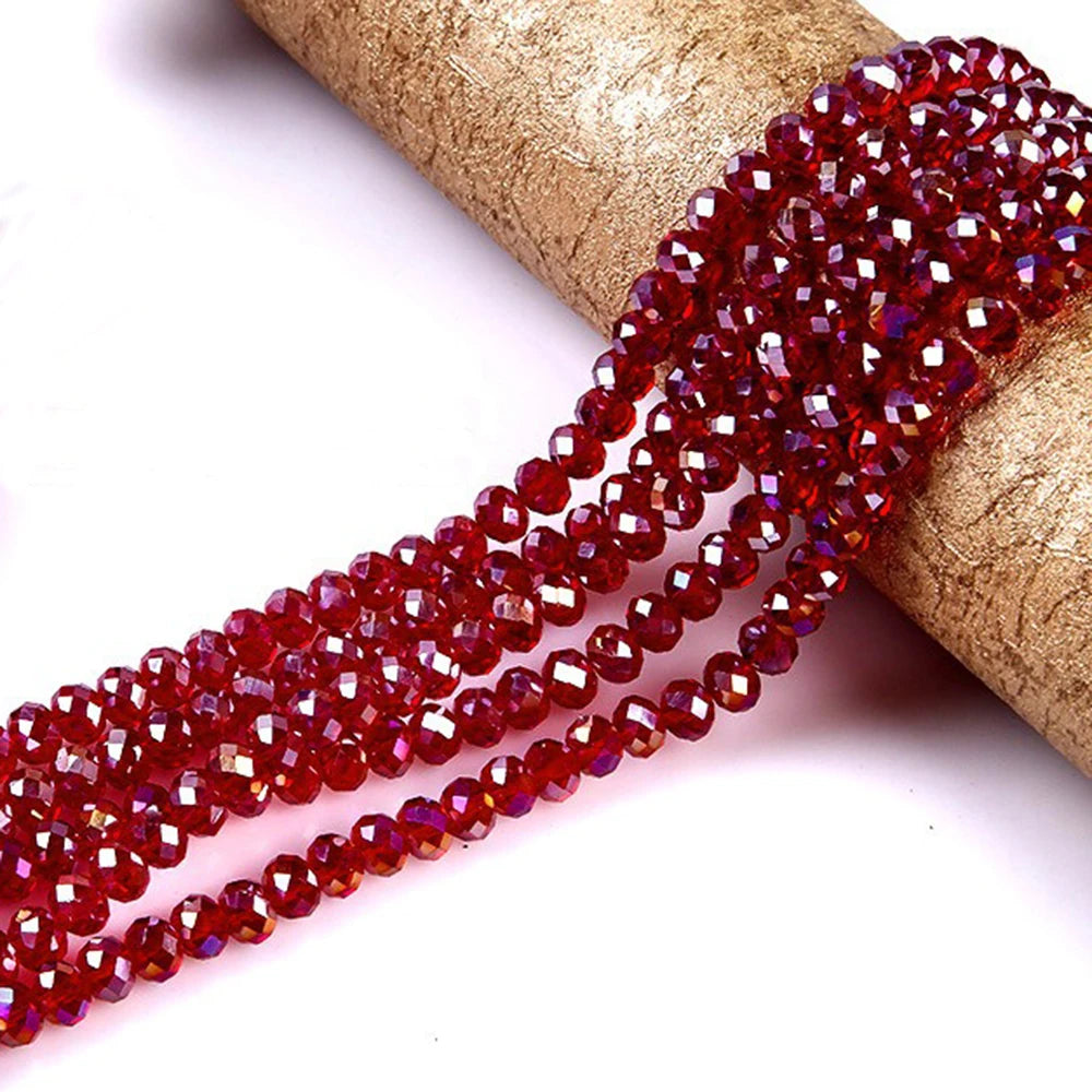 A strand of faceted red crystal glass spacer beads is draped over a gold-colored cylindrical object.