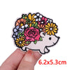 A hand holds a colorful embroidery patch featuring a pink and yellow floral design surrounding a cute white cartoon bear face