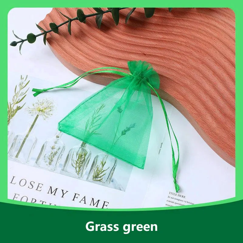 A green organza drawstring gift bag tied with a green ribbon resting on a wooden surface.