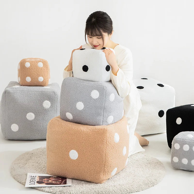 A person is holding a white polka-dotted plush pillow next to several gray and tan colored soft cushions.