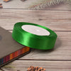 A roll of bright green lustrous satin ribbon with a white center, resting on a wooden surface next to a dark notebook.