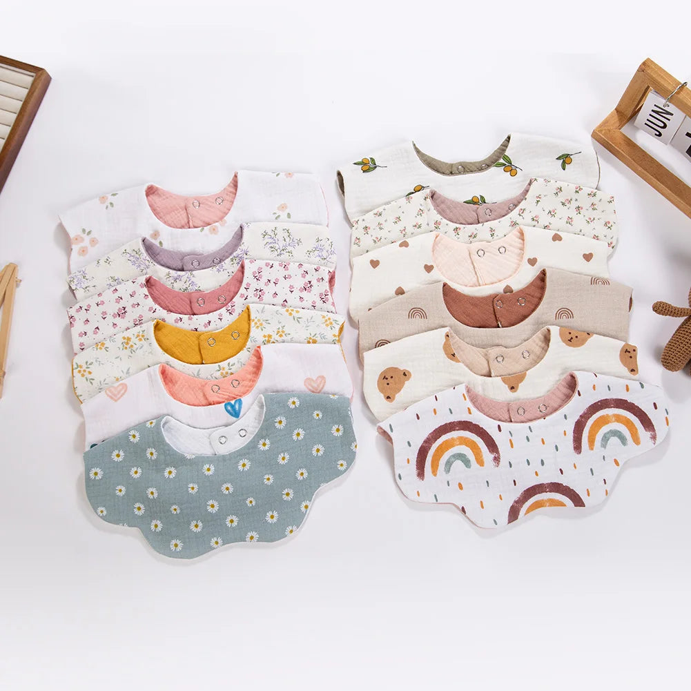 A collection of six-layer muslin cotton baby bibs and burp cloths in various pastel colors with adjustable snap closures.
