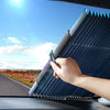 A hand is adjusting a pleated, blue retractable car windshield sunshade on a vehicle.