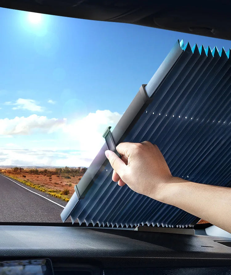 A hand is adjusting a pleated, blue retractable car windshield sunshade on a vehicle.