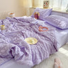 A purple breathable summer seersucker quilt spread on a bed with a white headboard and natural light.