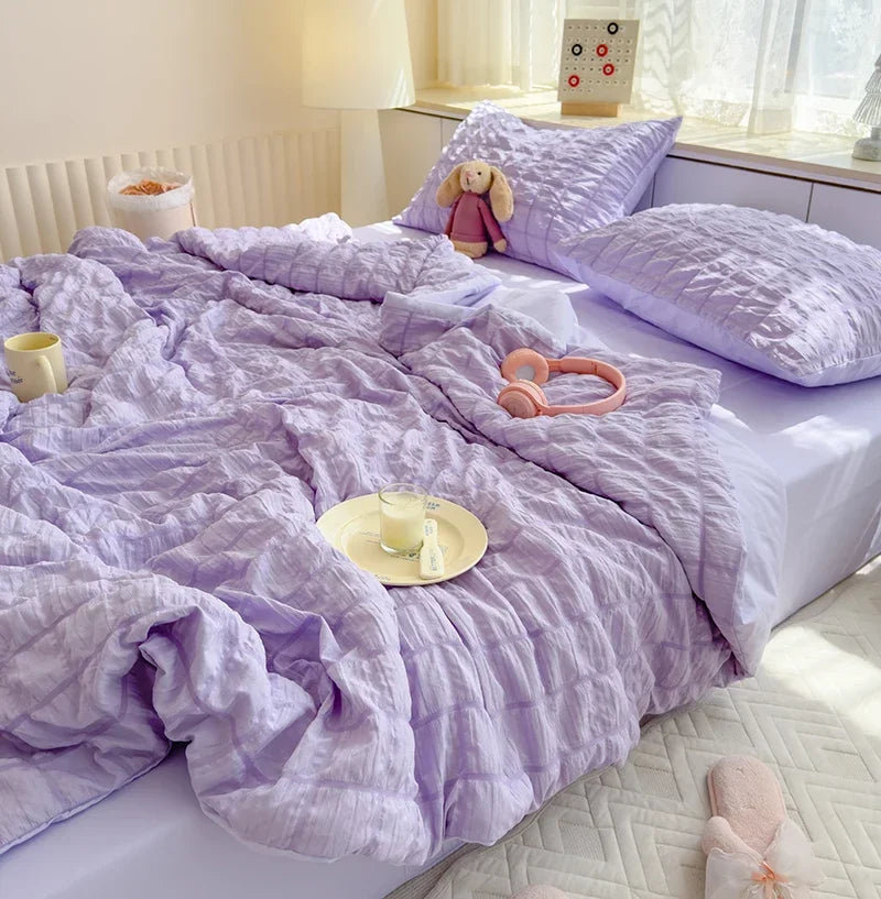 A purple breathable summer seersucker quilt spread on a bed with a white headboard and natural light.