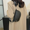 A woman is holding a black multi-pocket PU leather waist bag with an adjustable strap against a light beige coat.