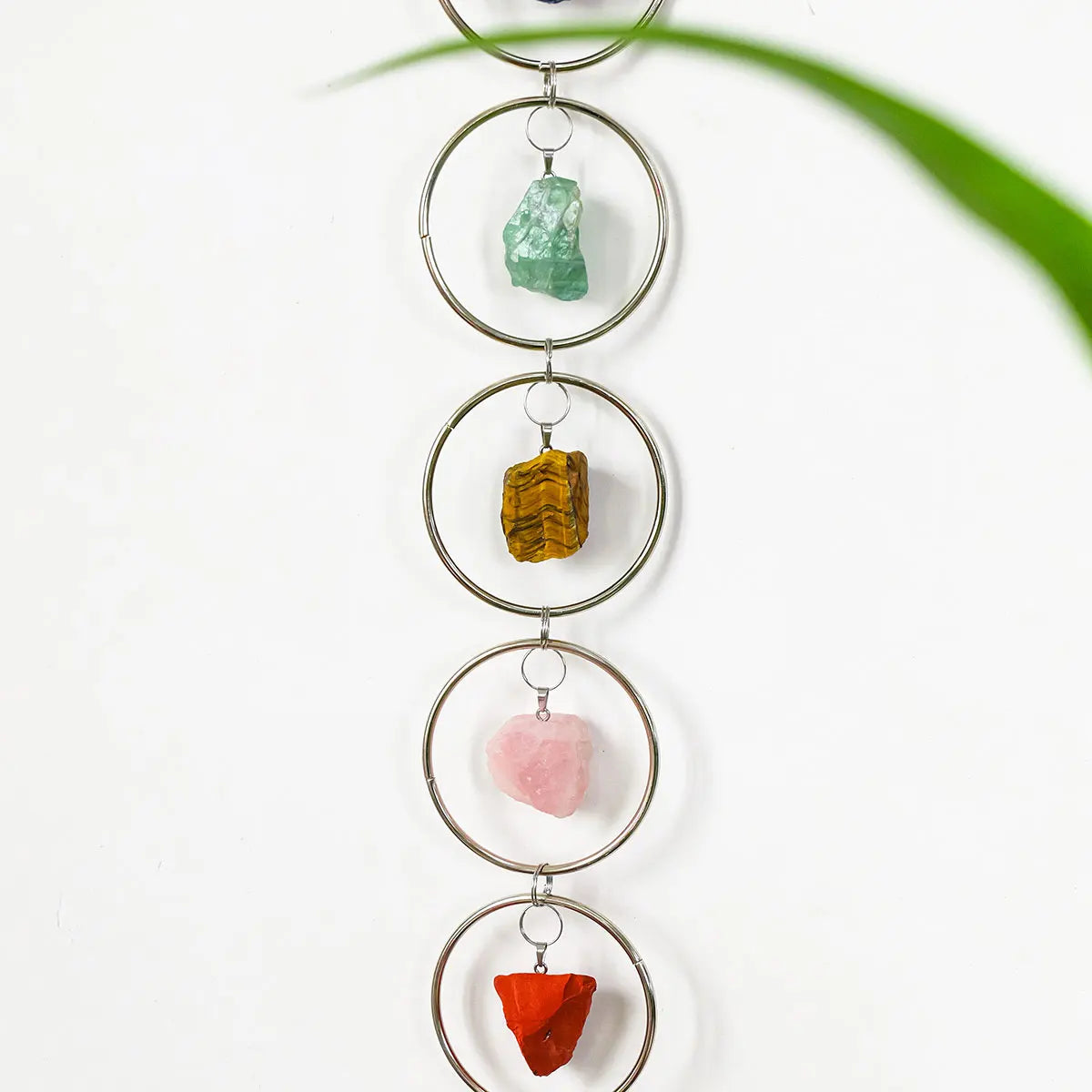 A hanging decoration featuring five polished crystals of varying colors, including green, yellow, pink, and red, suspended on