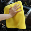 A hand is holding a bright yellow microfiber car cleaning towel in a car interior setting.