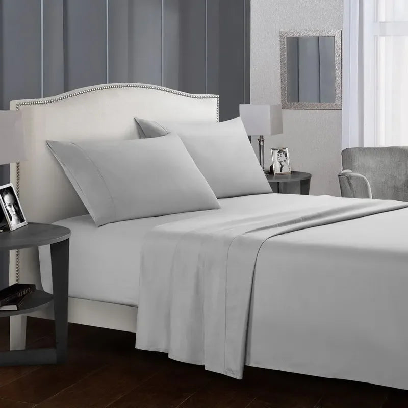 A white bed with soft gray bedding, including a fitted sheet, flat sheet, and pillows, in a modern bedroom setting.