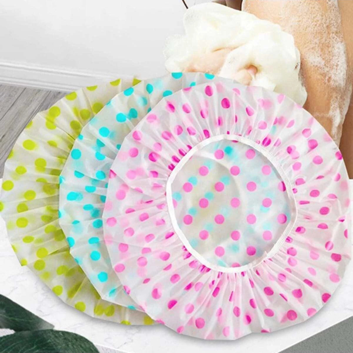 A pink polka-dotted disposable waterproof shower cap is shown next to other similar caps.