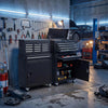 A dark gray rolling tool cabinet with a black tool chest and various tools stored inside in an industrial workshop.