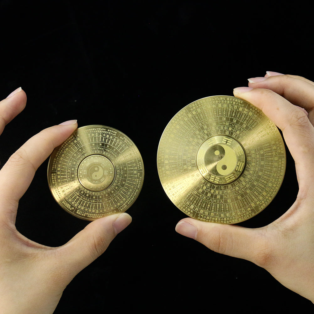 A hand holds a round solid brass Feng Shui compass featuring Yin Yang and eight trigrams against a black background.