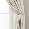 A close-up of a beige curtain being tied back with a silver iron curtain tieback hook.