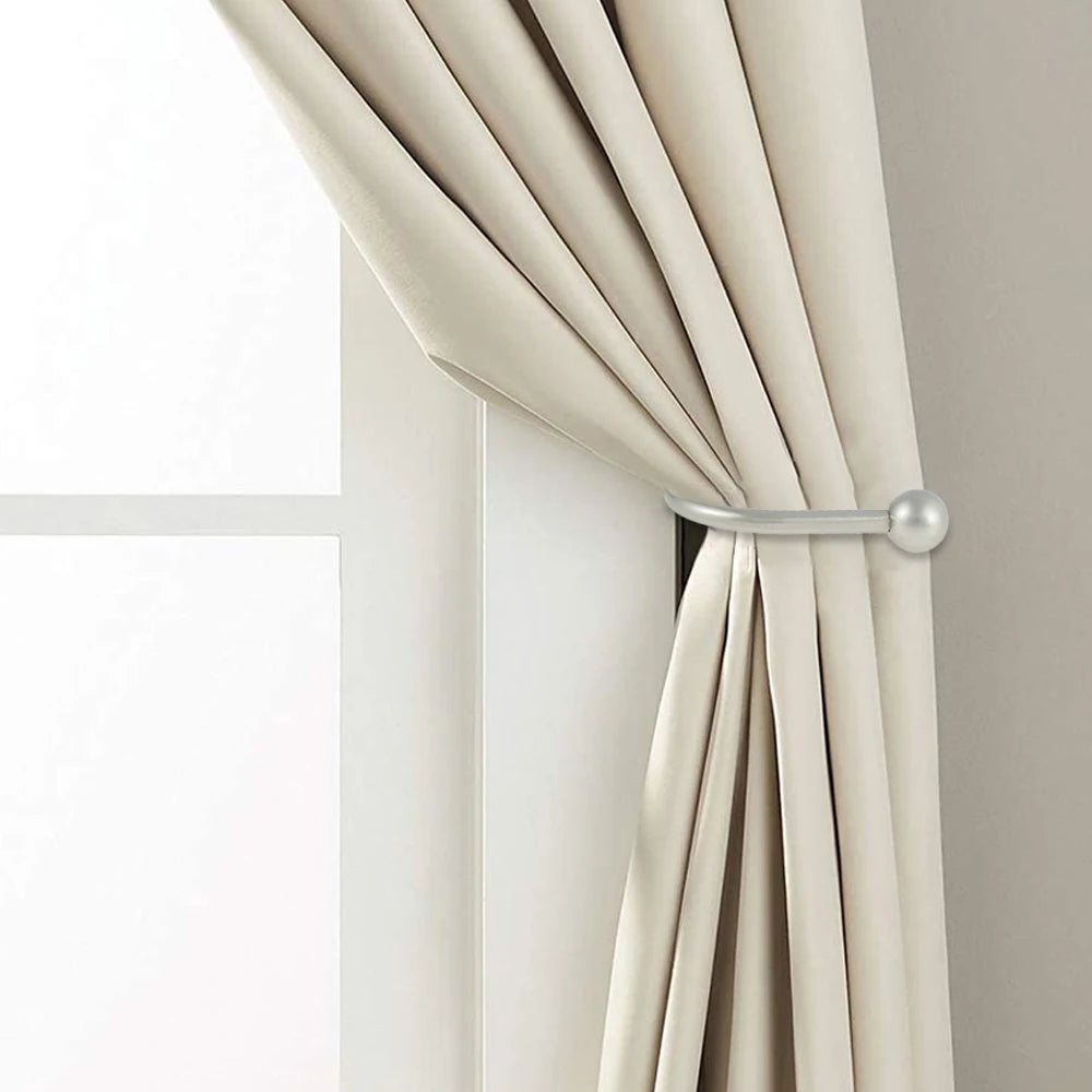 A close-up of a beige curtain being tied back with a silver iron curtain tieback hook.