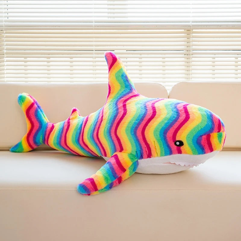 Buntes, gestreiftes riesiges Hai-Plüschtier liegt auf einem hellen Sofa.