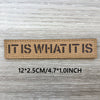 A brown woven patch with the text IT IS WHAT IT IS engraved on it, measuring 12x2.5cm or 4.7x1.0inch.
