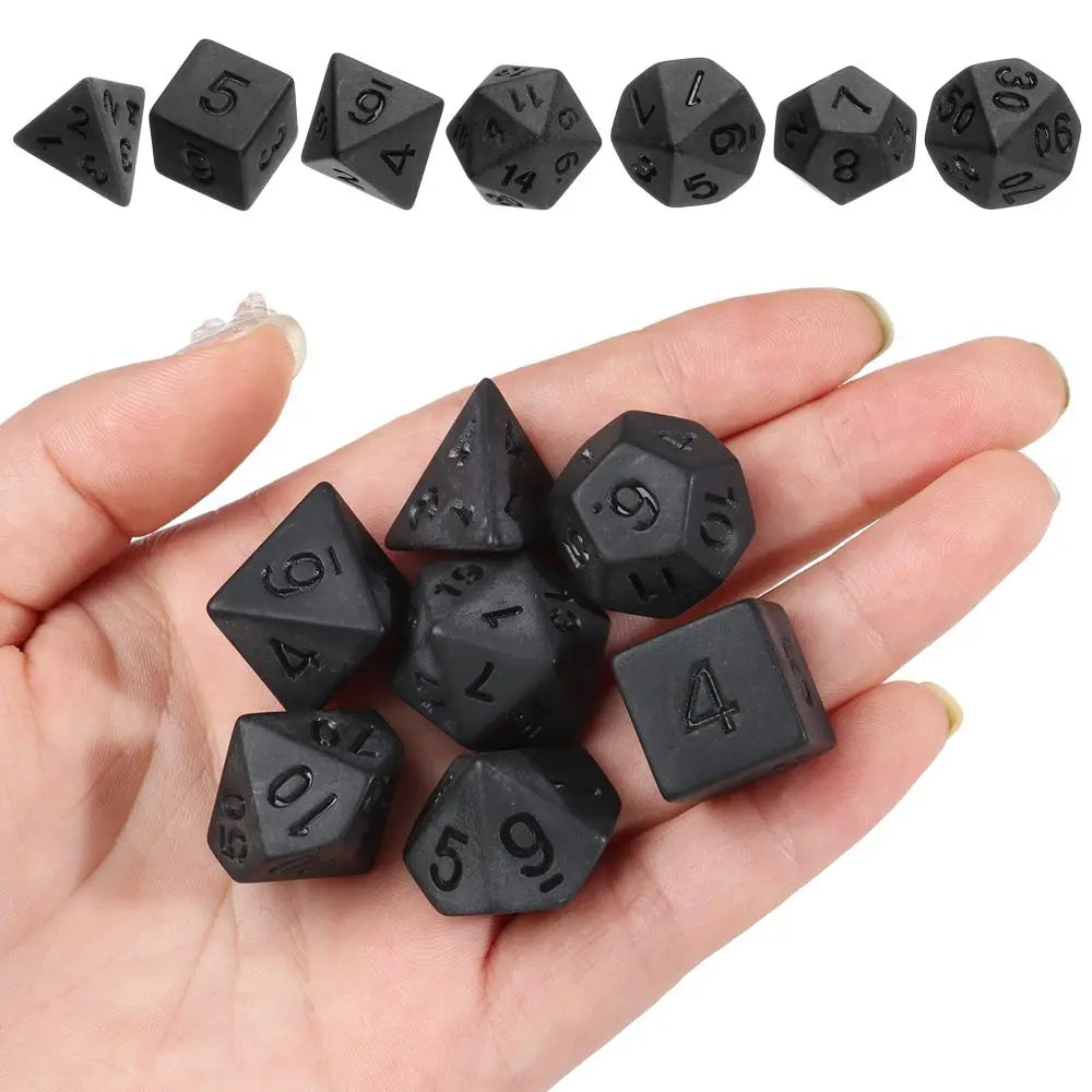 A hand holds a set of matte black polyhedral dice used for tabletop role-playing games.