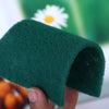 A hand holds a dark green microfiber kitchen scrub sponge, showing its texture and shape.