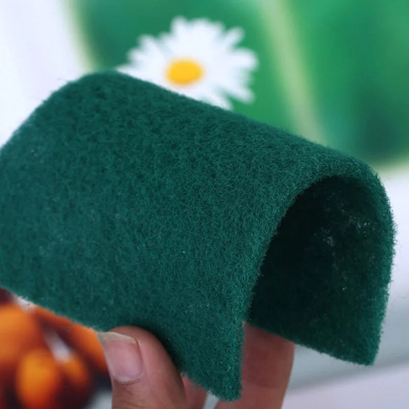 A hand holds a dark green microfiber kitchen scrub sponge, showing its texture and shape.