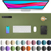 A computer monitor displays colorful graphics, surrounded by a green desk pad, a smartphone, keyboard, mouse, and a leather n