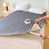 Grauer gesteppter wasserdichter Matratzen-Schutz auf einem Bett mit Kissen und einer Tasse.