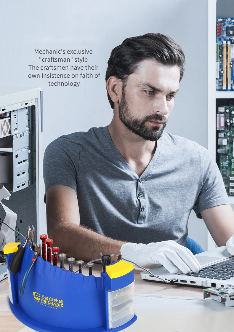A man working on a laptop with various repair tools and electronics organized in a blue desktop rack.