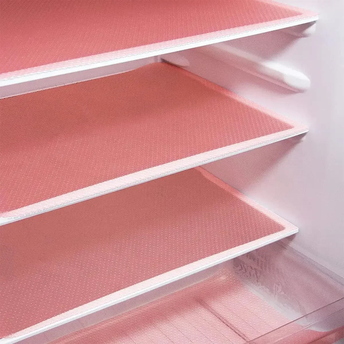 A close-up view of three pink EVA refrigerator shelf liners installed in a white cabinet.