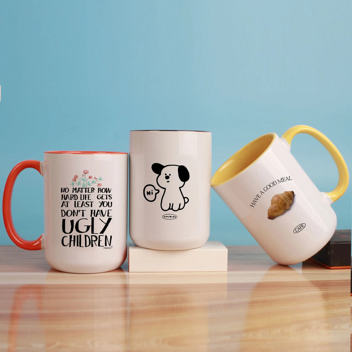 Three white ceramic coffee mugs of different sizes with black line drawings on them sitting on a wooden surface.