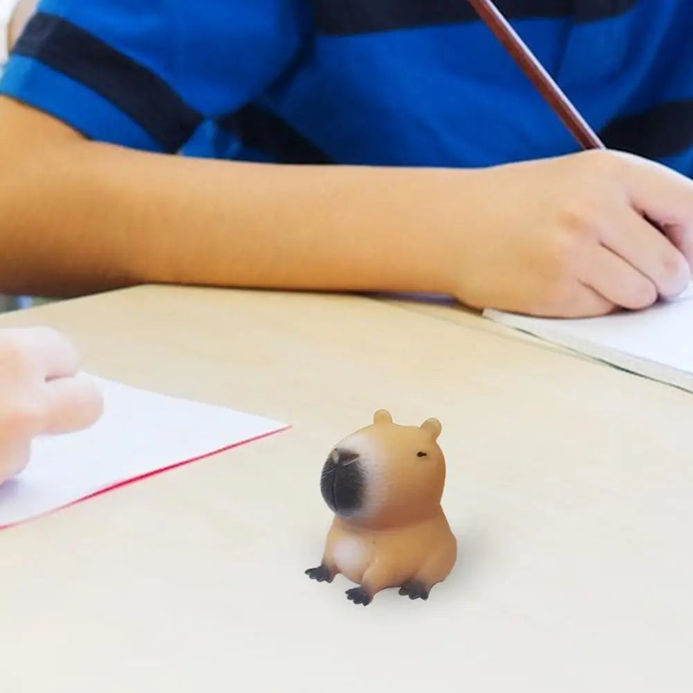 A small, brown cartoon capybara squeeze toy resting on a white table next to a piece of paper.