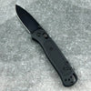 A black folding pocket knife with a drop point blade resting on a gray, textured surface.