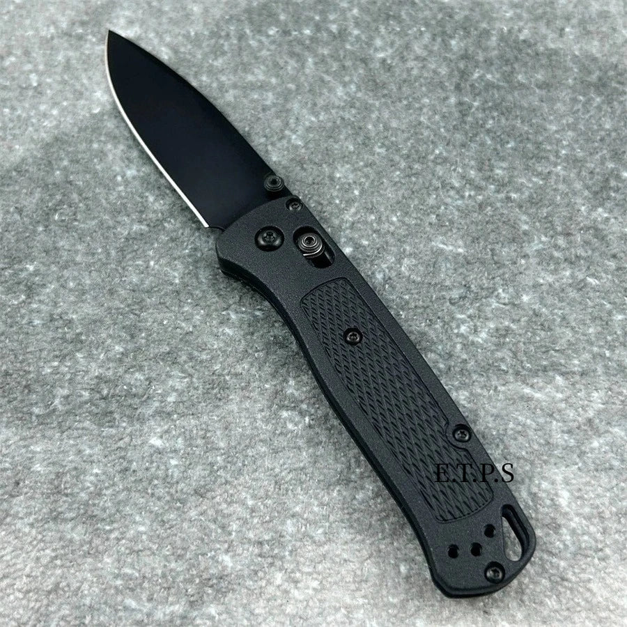 A black folding pocket knife with a drop point blade resting on a gray, textured surface.
