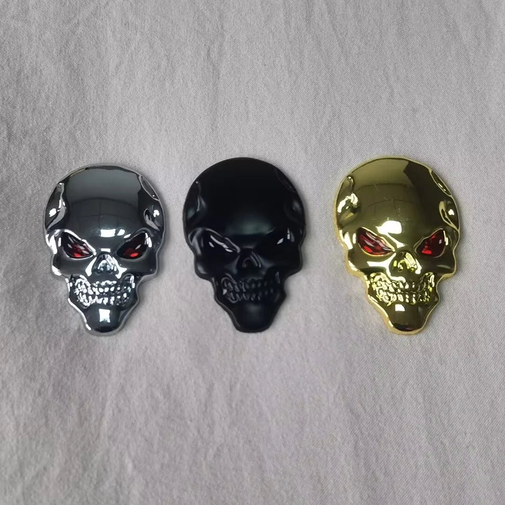 Three chrome skull emblems in silver, black, and gold on a white background.