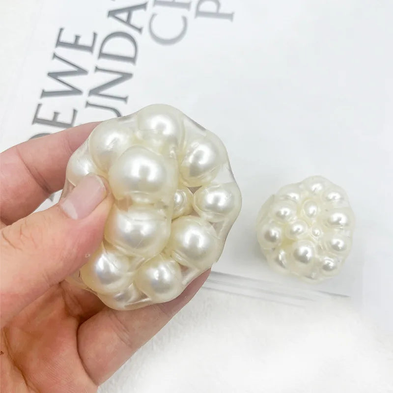 Eine Hand hält einen Haufen weißer Perlen, die als quichelbare Stressball dienen.