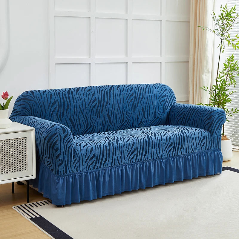 A deep blue jacquard sofa cover with a zebra stripe pattern and an elastic skirt displayed in a bright room.