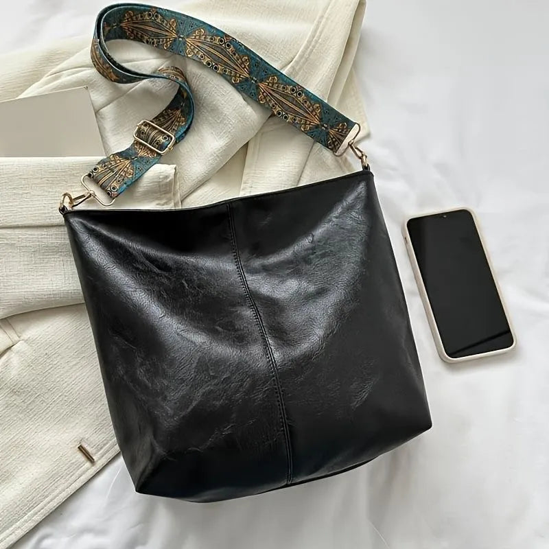 Black leather shoulder bag with a brown and gold embroidered strap resting on a white surface.