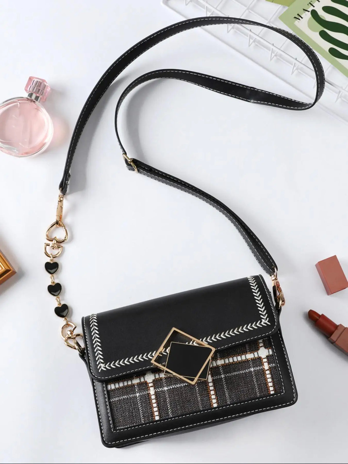 Schwarze Lederhandtasche mit goldenen Kettenerweiterungen und gemusterter Klappe auf weißem Untergrund.