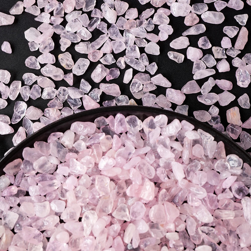 Pink rose quartz crystal gravel scattered on a dark surface.
