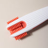 A white silicone baby bottle cleaning brush with orange bristles is shown against a light background.