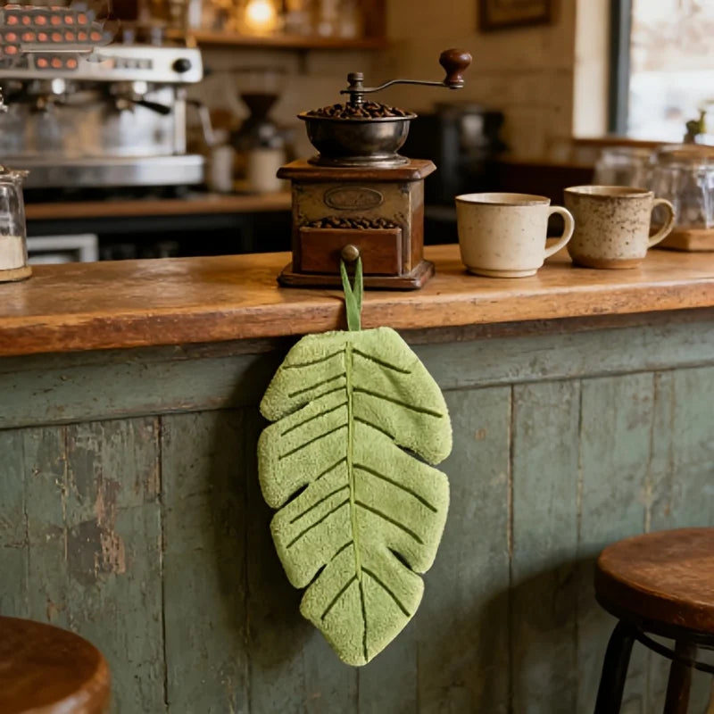 A green banana leaf absorbent hand towel hanging on a wooden counter in a cafe setting.