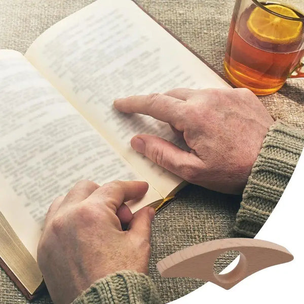 Eine Hand hält einen ergonomischen Holzseitenhalter, der eine Seite in einem offenen Buch auf einer strukturierten Stoffoberf