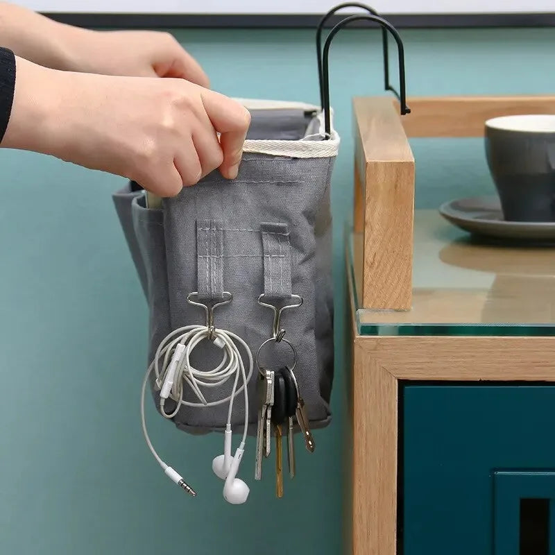 A hand is hanging a grey fabric storage organizer with multiple earphones and wires on a hook.