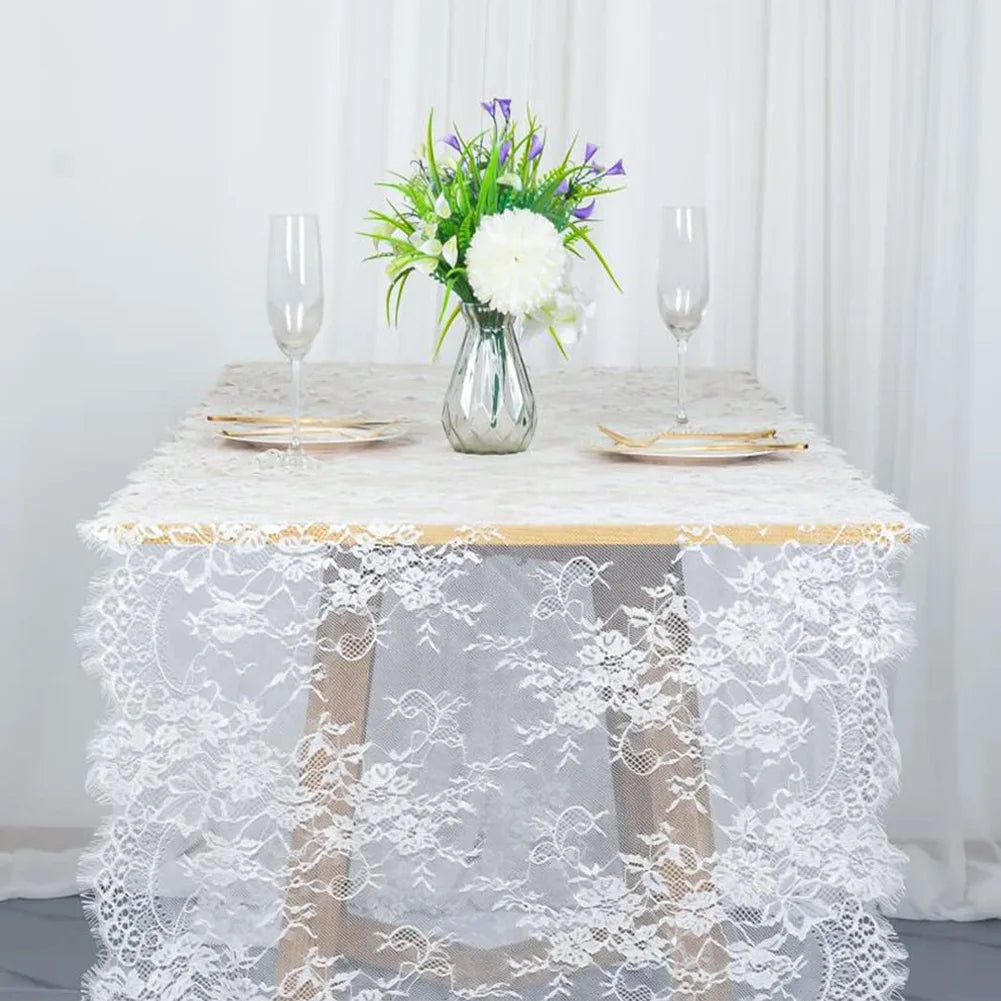 Vintage white embroidered floral lace table runner displayed on a table setting with a vase of greenery and white flowers.