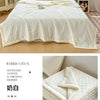 A white waffle-weave quilt with light yellow accents displayed on a bed in a bright room.